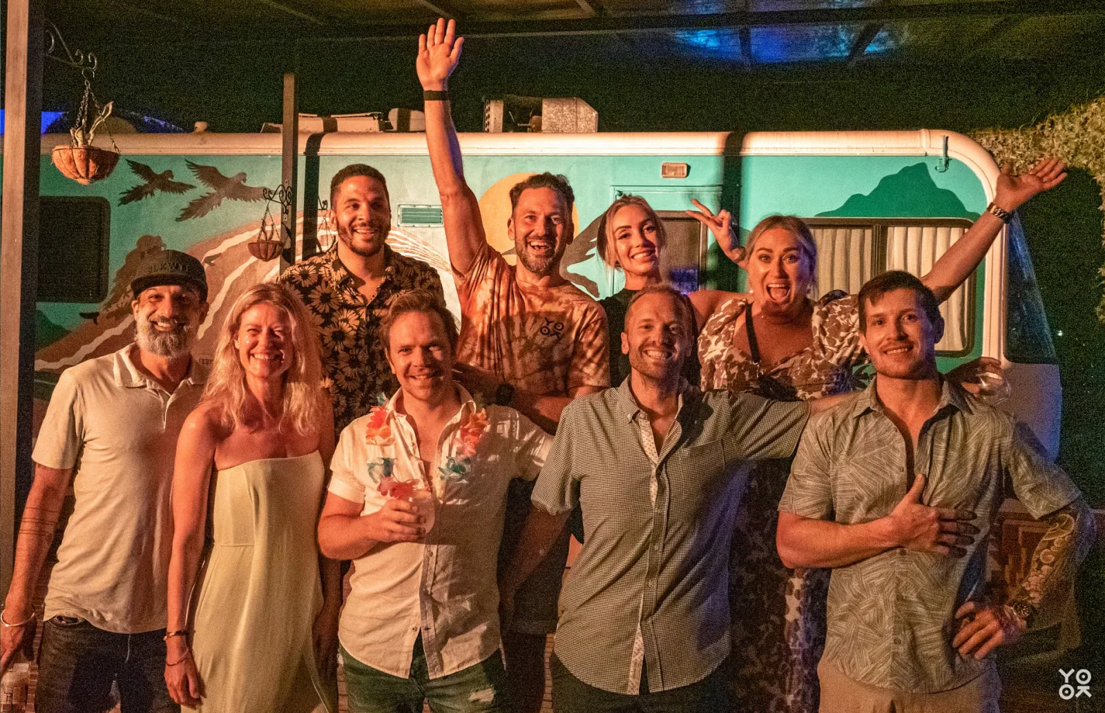 A group of friends posing together at night in front of a turquoise camper van
