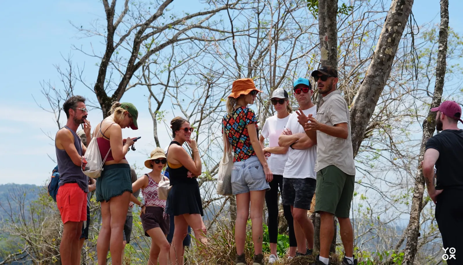 A group walking a sunlit hillside trail while a guide talks to them
