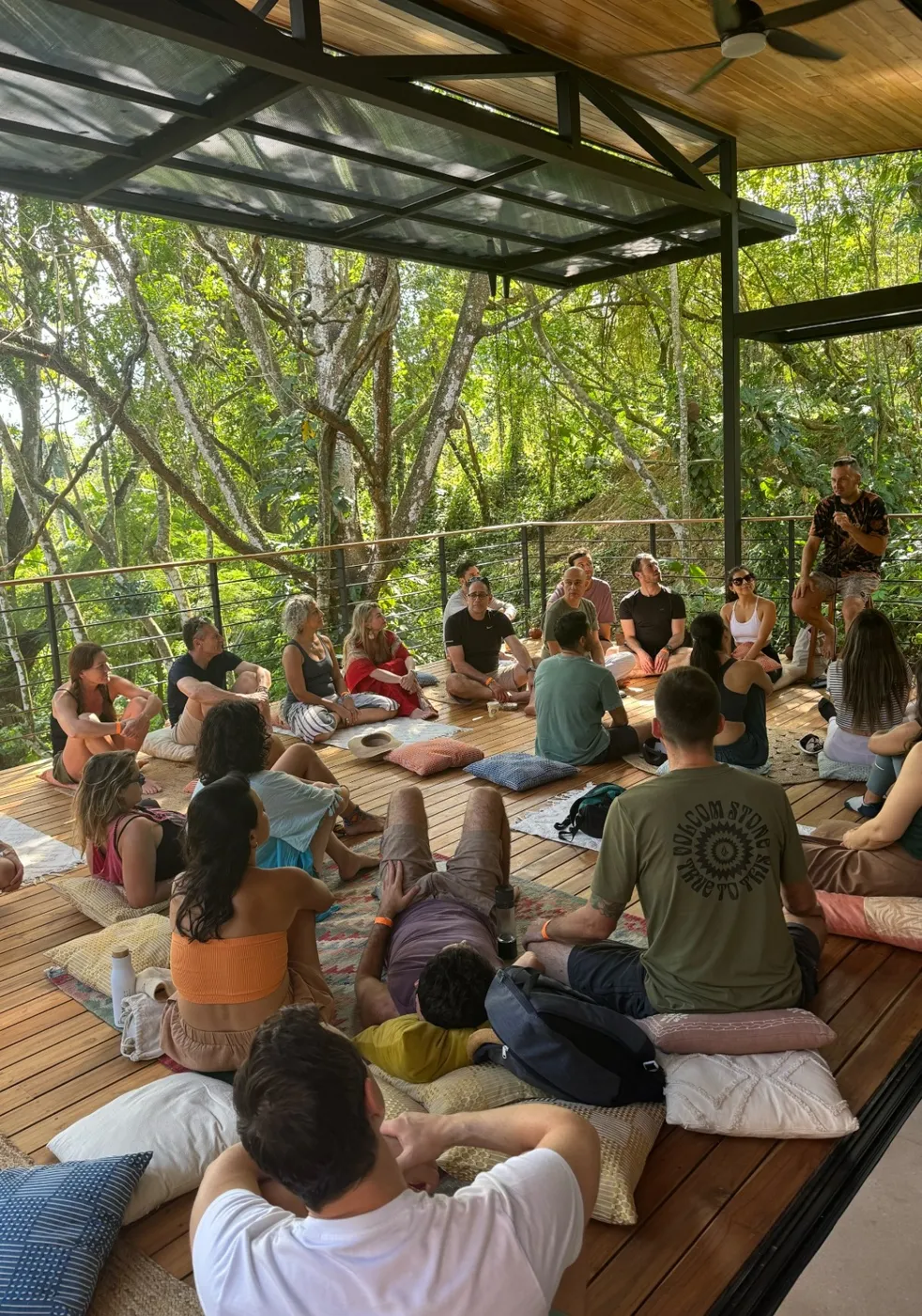 Oka community members in a circle on a covered jungle deck